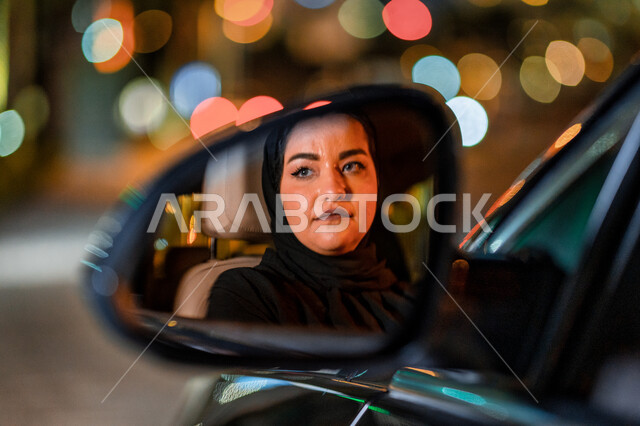 انعكاس لوجه سيده على مرآة السيارة الجانبية، اتقان المرأة لقيادة السيارة في الطرق العامة، صورة مقربة لسيدة عربية اماراتيه خليجية تجلس داخل سيارتها، مفهوم الحرية والاستقلال، شابة سعودية محجبة تنظر لشيء ما، القيادة بحذر واتباع قواعد الأمن والسلامة العامة.