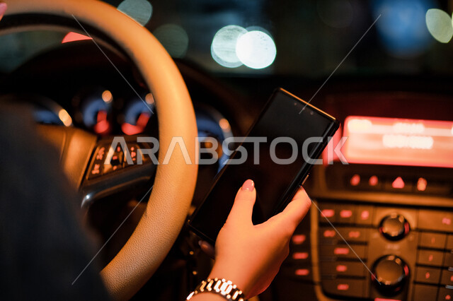  مفهوم الحرية والاستقلال الذاتي، سيدة اماراتيه تجلس داخل سيارتها تمسك الهاتف المحمول بيدها، القيادة في الشوارع والطرق العامة، صورة مقربة لإمرأة عربية خليجية سعودية تقوم بتتبع الطريق عبر الانترنت، اعتماد المرأه على نفسها في التنقل والمواصلات.