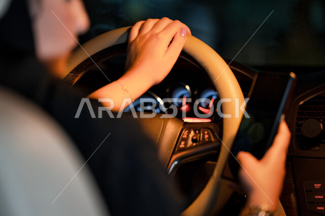 سيدة اماراتيه تجلس داخل سيارتها تحمل الهاتف المحمول، مفهوم الاعتماد على النفس والاستقلاليه، القيادة في الشوارع والطرق العامة، صورة مقربة لإمرأة عربية خليجية سعودية تقوم بتتبع الطريق عبر الانترنت، اعتماد المرأه على نفسها في التنقل والمواصلات.