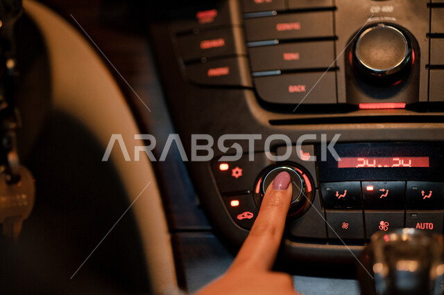 تحضير السيارة قبل القيادة في الطرق والشوارع العامة، صورة مقربة ليد سيده سعودية تقوم بتشغيل التكييف في سيارتها، مفهوم الاستقلال والحرية، اتباع قواعد السلامه، اعتماد المرأه على نفسها في التنقل، امرأه عربية خليجية اماراتيه تقوم بالضغط على زر المكيف.