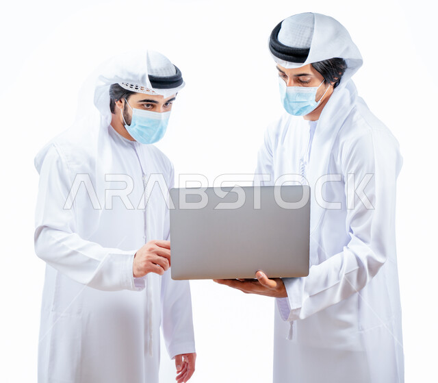 بورتريه لرجلان أعمال عربيان خليجيان اماراتيان يرتديان الكمامة الواقية، انجاز مهام العمل من خلال الحاسوب المحمول، نقاشات وحوارات عمل، متابعة العمل، بيئة العمل الاماراتي، الإشراف وتدقيق العمل، الالتزام باجراءات الوقاية من فايروس كورونا، خلفية بيضاء