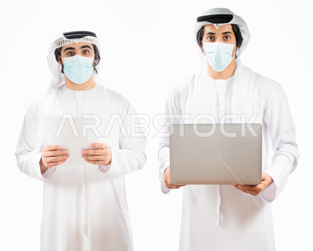 بورتريه لرجلان أعمال عربيان خليجيان اماراتيان يرتديان الكمامة الواقية، انجاز مهام العمل من خلال الحاسوب المحمول، نقاشات وحوارات عمل، متابعة العمل، بيئة العمل الاماراتي، الإشراف وتدقيق العمل، الالتزام باجراءات الوقاية من فايروس كورونا، خلفية بيضاء