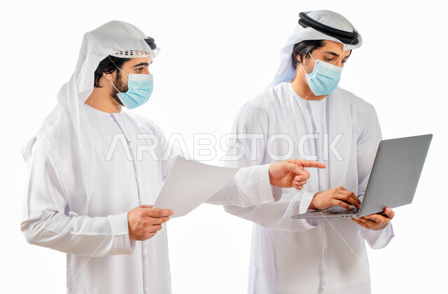 بورتريه لرجلان أعمال عربيان خليجيان اماراتيان يرتديان الكمامة الواقية، انجاز مهام العمل من خلال الحاسوب المحمول، نقاشات وحوارات عمل، متابعة العمل، بيئة العمل الاماراتي، الإشراف وتدقيق العمل، الالتزام باجراءات الوقاية من فايروس كورونا، خلفية بيضاء