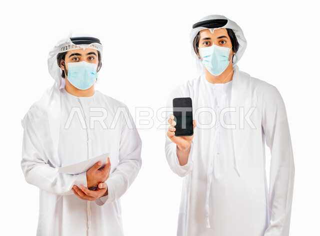 بورتريه لرجلان أعمال عربيان خليجيان اماراتيان يرتديان الكمامة الواقية، رجل يمسك بالهاتف المحمول، شاشة سوداء فارغة، عرض خدمات وتطبيقات الهاتف المحمول، التسوق الإلكتروني، الالتزام باجراءات الوقاية من فايروس كورونا، خلفية بيضاء