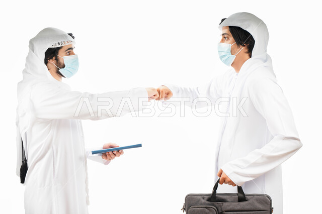 Portrait of two Arab Gulf Emirati businessmen wearing a muzzle and shaking hands, a business agreement between businessmen, a successful deal, cooperation in work, achieving work goals, adherence to precautionary measures against the Corona virus, a white