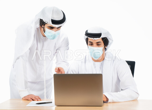 بورتريه لرجلان أعمال عربيان خليجيان اماراتيان يرتديان الكمامة الواقية، انجاز مهام العمل من خلال الحاسوب المحمول، نقاشات وحوارات عمل، متابعة العمل، بيئة العمل الاماراتي، الإشراف وتدقيق العمل، الالتزام باجراءات الوقاية من فايروس كورونا، خلفية بيضاء