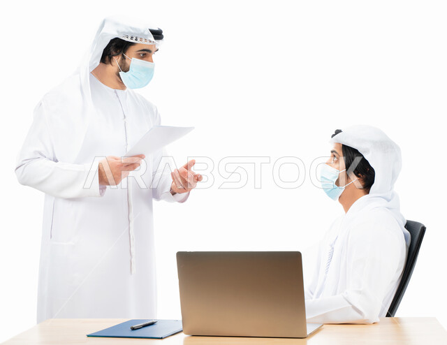 بورتريه لرجلان أعمال عربيان خليجيان اماراتيان يرتديان الكمامة الواقية، انجاز مهام العمل من خلال الحاسوب المحمول، نقاشات وحوارات عمل، متابعة العمل، بيئة العمل الاماراتي، الإشراف وتدقيق العمل، الالتزام باجراءات الوقاية من فايروس كورونا، خلفية بيضاء