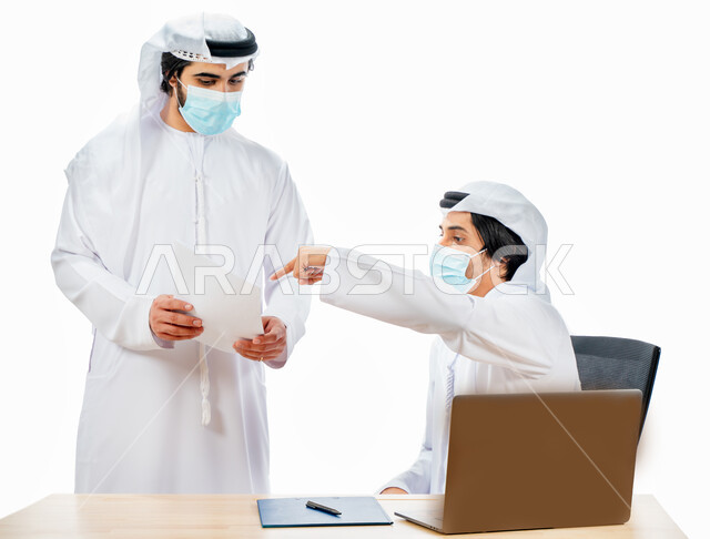 بورتريه لرجلان أعمال عربيان خليجيان اماراتيان يرتديان الكمامة الواقية، انجاز مهام العمل من خلال الحاسوب المحمول، نقاشات وحوارات عمل، متابعة العمل، بيئة العمل الاماراتي، الإشراف وتدقيق العمل، الالتزام باجراءات الوقاية من فايروس كورونا، خلفية بيضاء