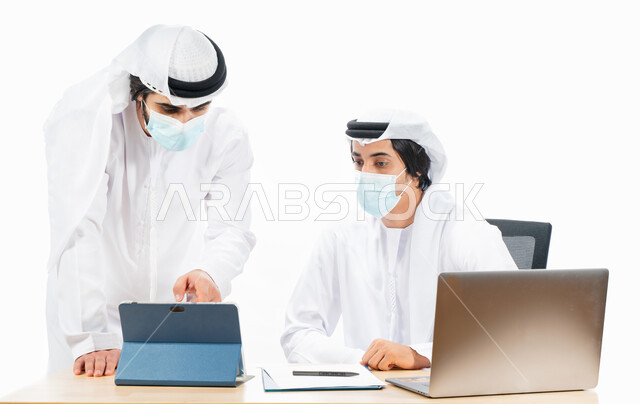 بورتريه لرجلان أعمال عربيان خليجيان اماراتيان يرتديان الكمامة الواقية، انجاز مهام العمل من خلال الحاسوب المحمول، نقاشات وحوارات عمل، بيئة العمل الاماراتي، استخدام جهاز التابليت في توضيح وتدقيق العمل، الالتزام باجراءات الوقاية من فايروس كورونا، خلفية بيضاء