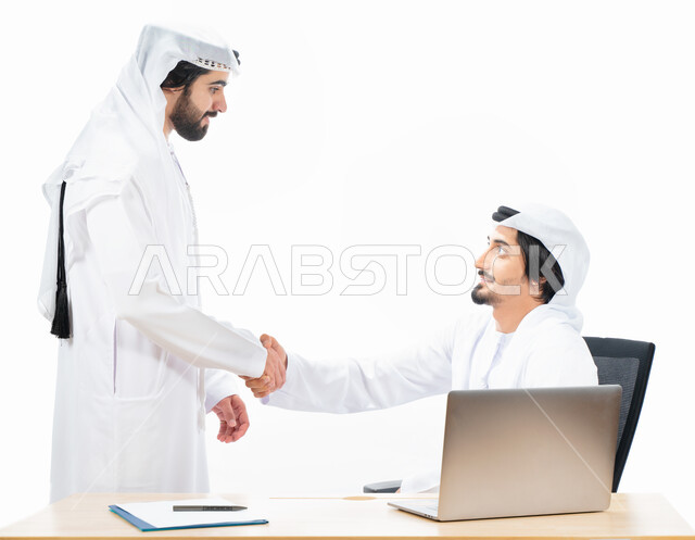 بورتريه لرجلان أعمال عربيان خليجيان اماراتيان يتصافحان، انجاز مهام العمل من خلال الحاسوب المحمول، نقاشات وحوارات عمل، زملاء عمل، بيئة العمل الاماراتي، الاشراف وتدقيق العمل، خلفية بيضاء