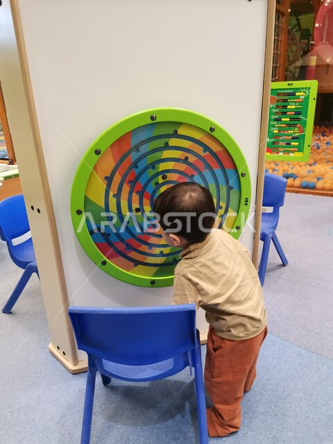 صورة من الخلف لطفل صغير يلعب بالألعاب الترفيهية ، ألعاب تعليمية ترفيهية ، تنمية قدرات و مهارات الطفل ، روضة أطفال ، حضانة أطفال ، أنشطة فنية وترفيهية  ، مراكز التنمية الفكرية
