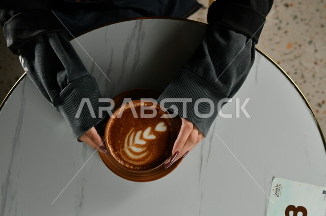 صورة مقربة ليدين إمرأه تمسك بفنجان القهوة برغوة كثيفة ، مشروب الكابتشينو الساخن ، مشروبات ساخنة لذيذة ، فنجان القهوة الساخن