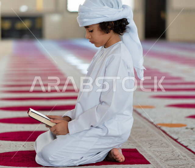 ولد صغير عربي خليجي إماراتي في أحد المساجد العربية، يحمل بيده كتاب القرآن الكريم، كتاب الله ، المصحف الشريف ، العبادة والتقرب الى الله، أماكن إسلامية مقدسة، إسلاميات وعبادة