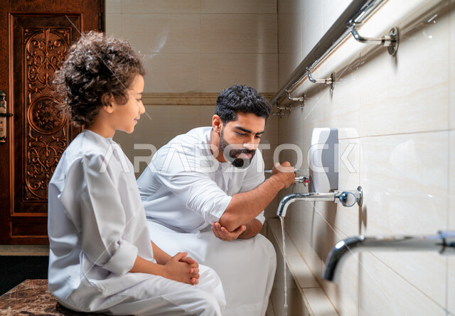 An Emirati Arab Gulf man and his son in places designated for ablution in an Arab mosque, learning how to ablution for children, purity and ablution, ablution sinks, basins and sinks for ablution, the concept of the pillars of ablution