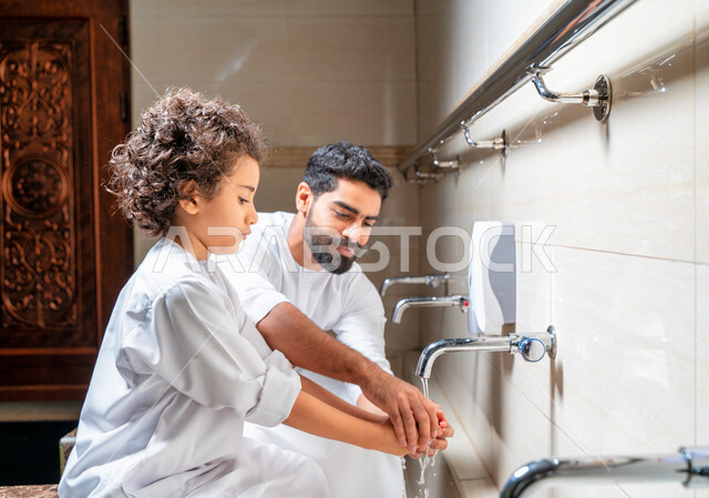 An Emirati Arab Gulf man and his son in places designated for ablution in an Arab mosque, learning how to ablution for children, purity and ablution, ablution sinks, basins and sinks for ablution, the concept of the pillars of ablution