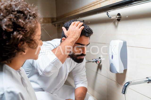 An Emirati Arab Gulf man and his son in places designated for ablution in an Arab mosque, learning how to ablution for children, purity and ablution, ablution sinks, basins and sinks for ablution, the concept of the pillars of ablution