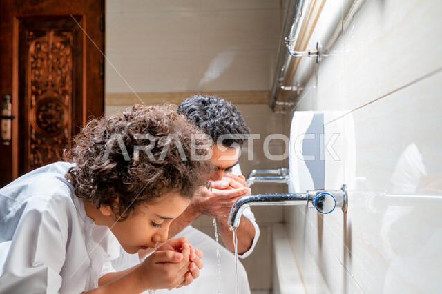 An Emirati Arab Gulf man and his son in places designated for ablution in an Arab mosque, learning how to ablution for children, purity and ablution, ablution sinks, basins and sinks for ablution, the concept of the pillars of ablution