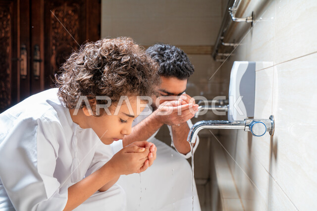 An Emirati Arab Gulf man and his son in places designated for ablution in an Arab mosque, learning how to ablution for children, purity and ablution, ablution sinks, basins and sinks for ablution, the concept of the pillars of ablution