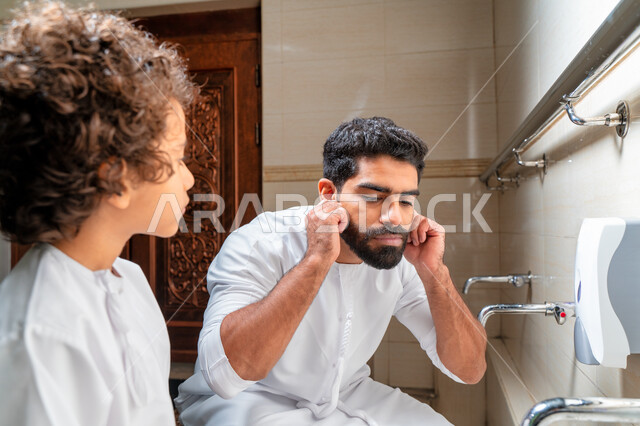 An Emirati Arab Gulf man and his son in places designated for ablution in an Arab mosque, learning how to ablution for children, purity and ablution, ablution sinks, basins and sinks for ablution, the concept of the pillars of ablution