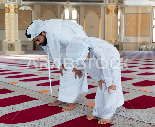 An Emirati Arab Gulf man and his son in an Arab mosque, performing the obligatory prayer, teaching prayer to children, worship and drawing closer to God, Islamic holy places, the concept of the pillars of Islam, kneeling in prayer, Islamism and worship