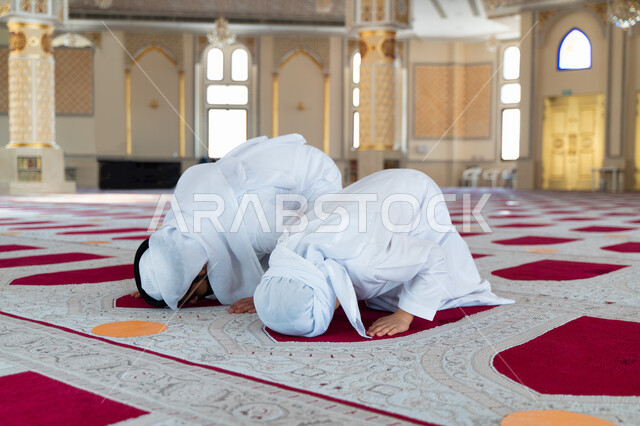An Emirati Arab Gulf man and his son in an Arab mosque, performing the obligatory prayer, prostrating in prayer, teaching prayer to children, worship and drawing closer to God, Islamic holy places, the concept of the pillars of Islam, Islamism and worship