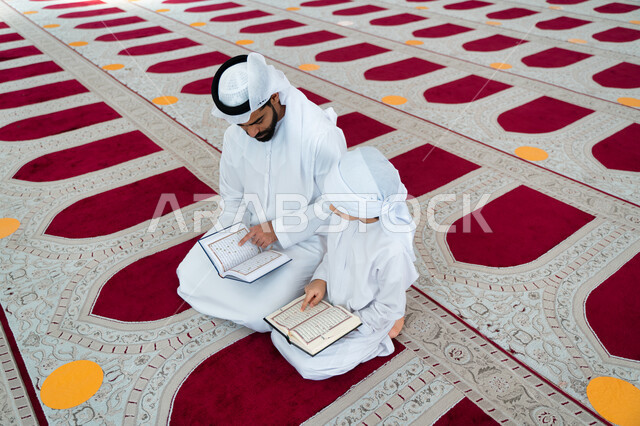 رجل عربي خليجي إماراتي وإبنه في أحد المساجد العربية، يحمل بيده المصحف الشريف ، قراءة القرآن الكريم ، تلاوة القرآن الكريم ، تحفيظ القرآن الكريم للأطفال ، العبادة والتقرب الى الله ، أماكن إسلامية مقدسة ، إسلاميات وعبادة