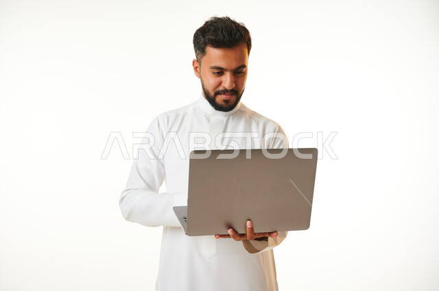 بورتريه لرجل عربي خليجي سعودي يحمل بيده جهاز الحاسوب المحمول، العمل عن بعد، انجاز مهام العمل، تصفح الانترنت، احتراف وظائف الحاسوب وتكنولوجيا المعلومات، خلفية بيضاء