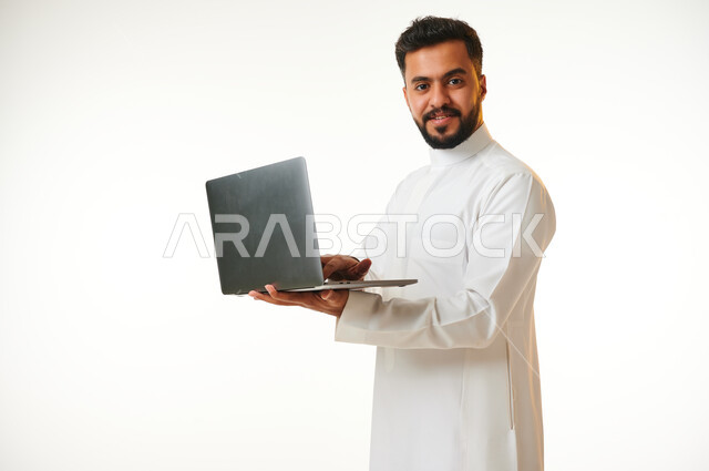 بورتريه لرجل عربي خليجي سعودي يحمل بيده جهاز الحاسوب المحمول، العمل عن بعد، انجاز مهام العمل، تصفح الانترنت، احتراف وظائف الحاسوب وتكنولوجيا المعلومات، خلفية بيضاء