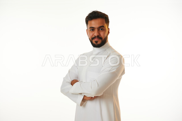 بورتريه لرجل عربي خليجي سعودي يقف مكتوف اليدين، ايدي متقاطعة، الوقوف بثقة، ايماءات وجه مبتسمة، خلفية بيضاء