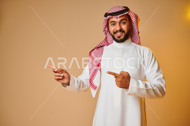 بورتريه لرجل عربي خليجي سعودي يشير باصبع السبابة نحو شيء ما، إيماءات وجه تدل على السعادة، الاشارة نحو شيء ما، خلفية ملونة