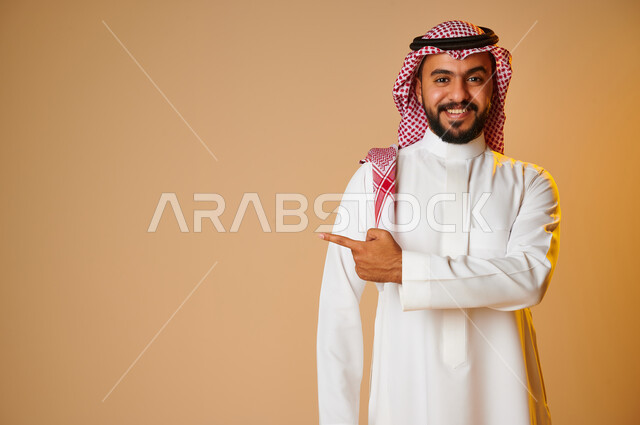 بورتريه لرجل عربي خليجي سعودي يشير باصبع السبابة نحو شيء ما، إيماءات وجه تدل على السعادة، الاشارة نحو شيء ما، خلفية ملونة