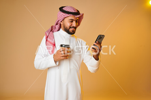 بورتريه لشاب عربي خليجي سعودي بيده كوب ويستخدم الهاتف المحمول، الاستمتاع بالمشروبات ساخنة، التسوق الالكتروني، طلبات اونلاين، التسوق الذكي، عملية شراء الكترونية، خدمات التوصيل السريع للمشروبات الساخنة، تصفح المواقع الالكترونية، خلفية ملونة