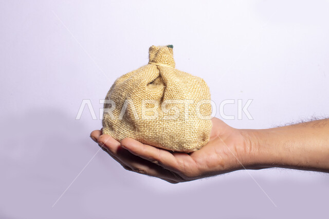 صورة مقربة ليد رجل يحمل كيس الخيش، مفهوم الدقة والزكاة، قماش الخيش، كيش محكم الاغلاق، قماش خشن، خلفية بيضاء