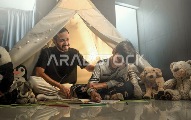 التخييم داخل المنزل, أب مع ابنه عربيان سعوديان خليجيان يجلسان داخل خيمة في المنزل,  قضاء وقت ممتع في اللعب مع الابناء , ايماءات تدل على السعادة والفرح,  أنشطة ترفيهية قبل النوم, الاهتمام بتربية وتعليم الابناء .