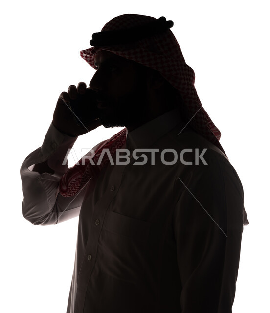 بورتريه ، صورة ظلية لرجل عربي خليجي سعودي ، إجراء مكالمة هاتفية بإستخدام الهاتف المحمول ، إستخدام اجهزة تقنية حديثة ، الإتصال والدردشة ، التواصل الإجتماعي ، خلفية بيضاء
