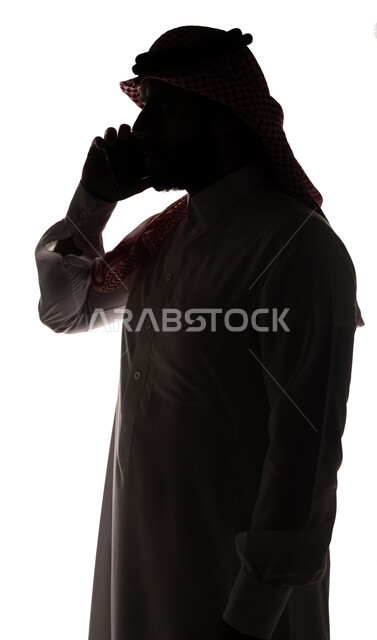 بورتريه ، صورة ظلية لرجل عربي خليجي سعودي ، إجراء مكالمة هاتفية بإستخدام الهاتف المحمول ، إستخدام اجهزة تقنية حديثة ، الإتصال والدردشة ، التواصل الإجتماعي ، خلفية بيضاء