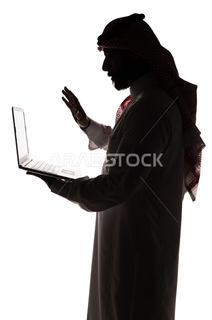 بورتريه ، صورة ظلية لرجل عربي خليجي سعودي ، إجراء مكالمة فيديو بإستخدام جهاز الحاسوب المحمول ، بث مباشر ، تصفح الإنترنت ، إستخدام اجهزة تقنية حديثة ، العمل عن بعد ، التسويق الإلكتروني ، مهن ووظائف ، عقد إجتماع عمل عبر اللابتوب ، خلفية بيضاء