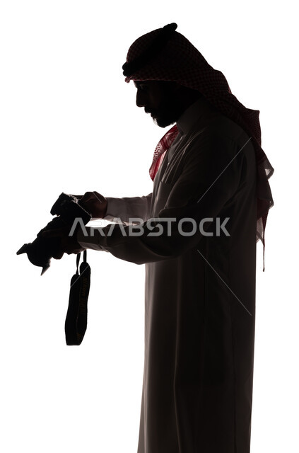 بورتريه ، صورة ظلية لرجل عربي خليجي سعودي ، يحمل بيده كاميرا تصوير عالية الدقة ، إلتقاط الصور التذكارية ، مصور سعودي ، إحتراف التصوير ، كاميرا عالية الدقة ، هواية التصوير ، خلفية بيضاء