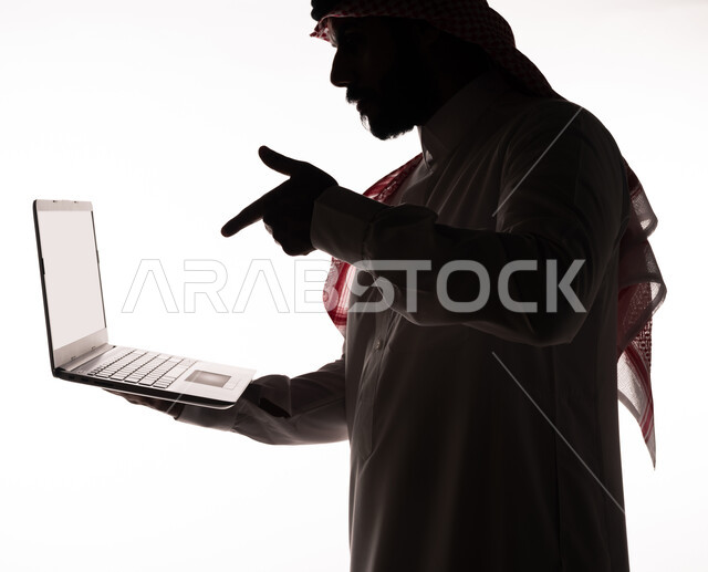 بورتريه ، صورة ظلية لرجل عربي خليجي سعودي ، إجراء مكالمة فيديو بإستخدام جهاز الحاسوب المحمول ، بث مباشر ، تصفح الإنترنت ، إستخدام اجهزة تقنية حديثة ، العمل عن بعد ، التسويق الإلكتروني ، مهن ووظائف ، عقد إجتماع عمل عبر اللابتوب ، خلفية بيضاء