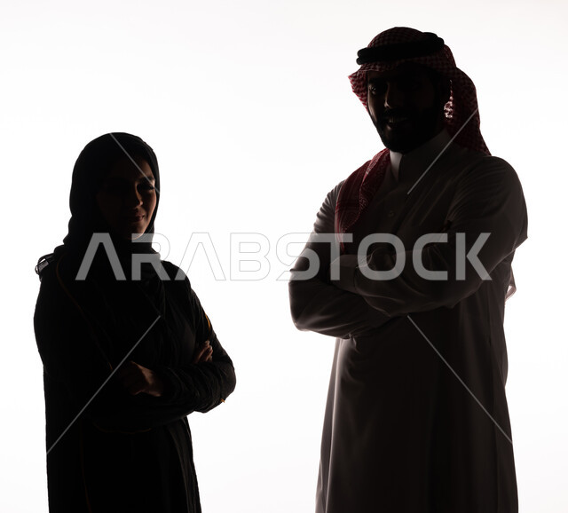 بورتريه ، صورة ظلية لزوجان عربيان خليجيان سعوديان ، يقفان بإستقامة ، بإيدي متقاطعة ، ينظران إلى الكاميرا ، خلفية بيضاء