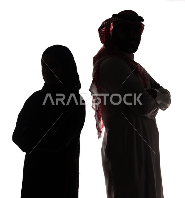 بورتريه ، صورة ظلية لزوجان عربيان خليجيان سعوديان ، يقفان بإستقامة ، بإيدي متقاطعة ، ينظران إلى الكاميرا ، خلفية بيضاء