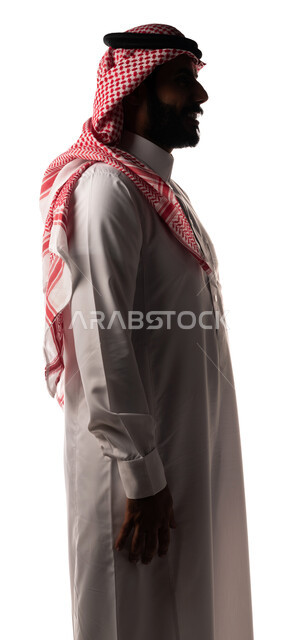 بورتريه بزاوية من الجنب لرجل عربي سعودي خليجي ، يرتدي الزي السعودي التقليدي ، يقف بإستقامه ، ينظر إلى الكاميرا ، تعابير وجه تدل على السعادة ، خلفية بيضاء