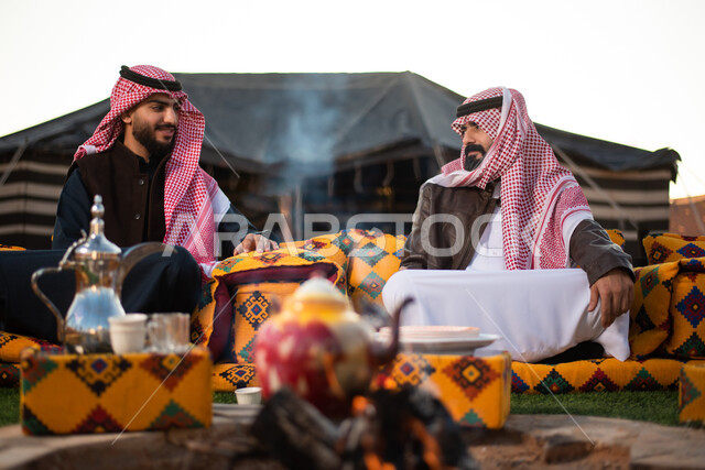 شابان عربيان خليجيان سعوديان يستمتعان برحلة تخييم برية في صحراء السعودية، ارتداء ملابس الشتاء الدافئة، حسن الضيافة والإستقبال، حوارات ونقاشات بين الاصدقاء، جلسة بر عربية شعبية مع شعلة الحطب، كشتة بر شبابية، مخيمات سياحية في الصحراء