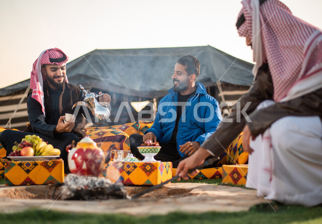 اصدقاء خليجيين سعوديين عرب يستمتعون برحلة بر برية في الصحراء، اشعال النار بالحطب، تقديم القهوة الساخنة للضيوف، حسن الضيافة والإستقبال، جلسة بر عربية شعبية، خيام شعبية في صحاري السعودية، كشتة بر شبابية