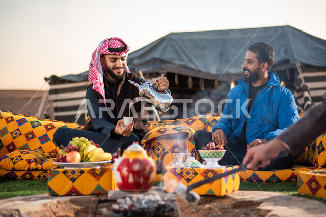 Saudi Gulf Arab friends enjoying a wild trip in the desert, offering hot coffee to guests, good hospitality and reception, lighting a fire with wood, a popular Arab session, popular tents in the deserts of Saudi Arabia, a youthful burial kashta