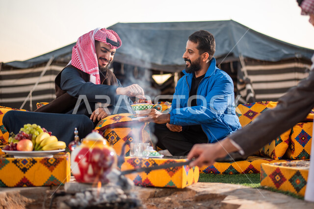 اصدقاء عرب خليجيين سعوديين يستمتعون برحلة بر برية في الصحراء، تقديم القهوة الساخنة للضيوف، حسن الضيافة والإستقبال، اشعال النار بالحطب، جلسة بر عربية شعبية، خيام شعبية في صحاري السعودية، كشتة بر شبابية