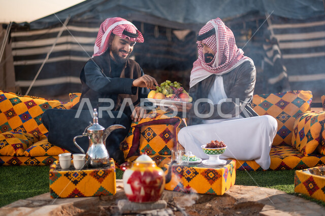 اصدقاء خليجيين سعوديين عرب يستمتعون برحلة بر برية في الصحراء، تقديم الفواكه للضيوف، حسن الضيافة والإستقبال، جلسة بر عربية شعبية، خيام شعبية في صحاري السعودية، كشتة بر شبابية