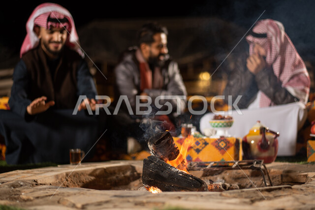 مجموعة من الاصدقاء العرب الخليجيين السعوديين يرتدون ملابس الشتاء الدافئة بايماءات تدل على البرد الشديد، التدفئة من خلال شعلة النار، حوارات ونقاشات بين الاصدقاء، خيام شعبية في صحاري السعودية، كشتة بر شبابية مسائية، اجواء شتوية ليلية