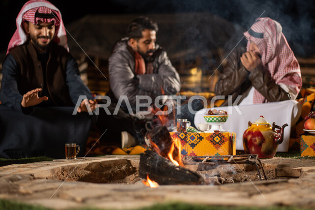 مجموعة من الاصدقاء العرب الخليجيين السعوديين بايماءات تدل على البرد الشديد، ارتداء ملابس الشتاء الدافئة، التدفئة من خلال شعلة النار، حوارات ونقاشات بين الاصدقاء، خيام شعبية في صحاري السعودية، كشتة بر شبابية مسائية، اجواء شتوية ليلية