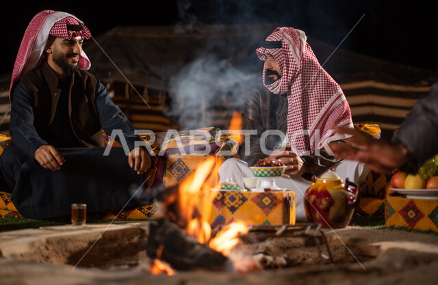 مجموعة من الاصدقاء العرب الخليجيين السعوديين بايماءات تدل على البرد الشديد، ارتداء ملابس الشتاء الدافئة، التدفئة من خلال شعلة النار، حوارات ونقاشات بين الاصدقاء، خيام شعبية في صحاري السعودية، كشتة بر شبابية مسائية، اجواء شتوية ليلية